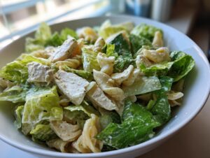 Close-up of a bowl filled with high protein chicken caesar pasta salad, featuring romaine lettuce, pasta, and creamy dressing.