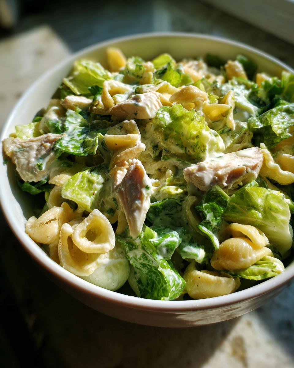 Close-up of a bowl filled with high protein chicken caesar pasta salad featuring pasta, chicken chunks, and creamy dressing.