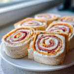 Close-up of several cross-sections of Italian pinwheel sandwiches showing layers of cream cheese, salami, and orange spread.