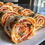 Close-up of sliced Italian pinwheels with cream cheese, salami, and herbs on a white plate.