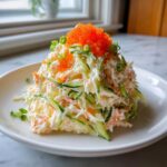 A mound of creamy japanese crab salad mixed with shredded cucumber and topped with bright orange tobiko fish roe.