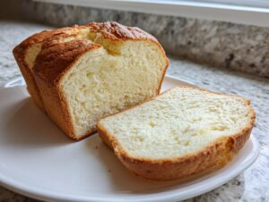 A golden-brown loaf of keto cottage cheese bread, partially sliced, resting on a white plate.