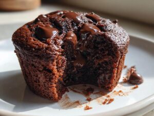 Close-up of a rich, dark chocolate muffin with melted chocolate chips oozing out, showing a moist interior.