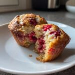A raspberry white chocolate muffin cut in half showing the moist crumb and bright red raspberries inside.