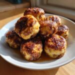 A stack of golden brown, glazed sausage mcgriddle bites resting in syrup on a white plate.