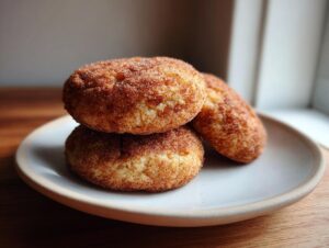 Three freshly baked snickerdoodle cookies stacked slightly on a light ceramic plate.