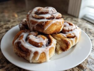 A stack of four soft sourdough cinnamon rolls generously topped with white icing on a white plate.