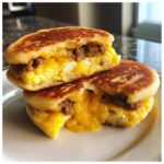 Two halves of a sourdough discard mcgriddle bites sandwich stacked, showing melted cheese, egg, and sausage filling.