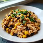 A close-up of a bowl filled with southwest crockpot chicken and rice, black beans, and corn, topped with cilantro.
