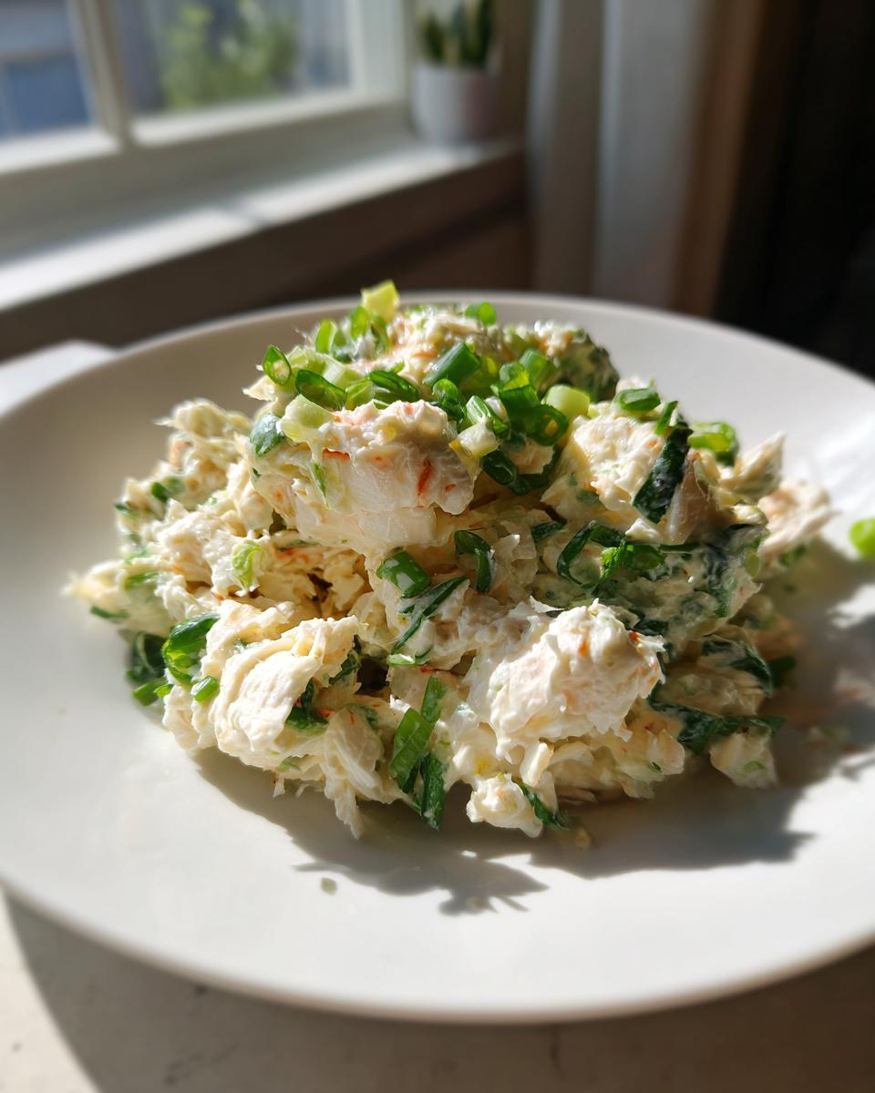 A mound of creamy spicy crab salad garnished generously with freshly chopped green onions on a white plate.
