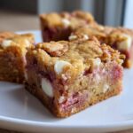 A close-up of a chewy strawberry cake mix cookie bars square showing pink strawberry filling and white chocolate chips.