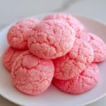 A close-up stack of bright pink, crinkly 3 ingredient strawberry cake mix cookies on a white plate.