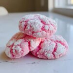 Three bright pink strawberry cake mix cookies heavily coated in cracked powdered sugar.