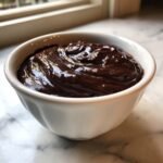 A close-up of thick, glossy homemade chocolate sauce filling a small white bowl.