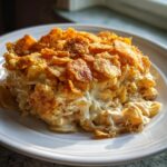 A serving of creamy tuna noodle casserole with potato chips topping on a white plate.