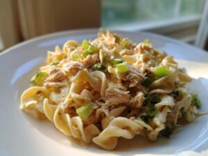 Close-up of a serving of creamy tuna noodle salad cold, mixed with pasta and topped with chopped green onions.