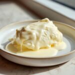 A scoop of ice cream or dessert covered in rich, smooth white chocolate sauce.