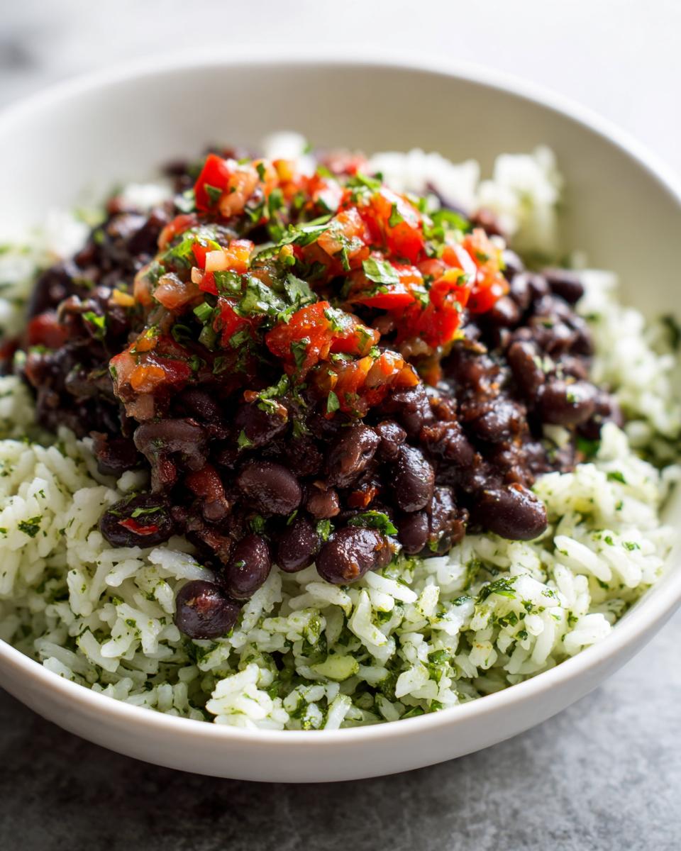 A close-up of a white bowl filled with cilantro lime rice, topped with seasoned black beans and fresh pico de gallo, making a perfect black bean and rice bowl.