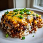 A hearty serving of black bean and rice casserole topped with melted cheddar cheese and sliced green onions.