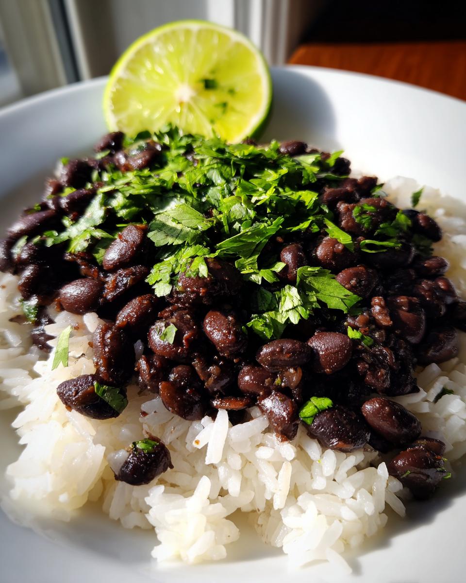 Close-up of a bowl of white rice topped with seasoned black beans and fresh cilantro, garnished with a lime half.
