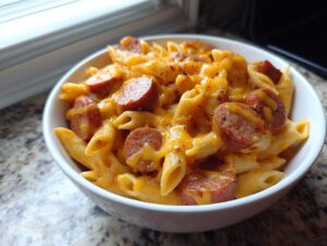 Close-up of a bowl of cheesy kielbasa pasta featuring penne noodles and sliced smoked sausage.