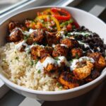 A close-up of a delicious chipotle chicken burrito bowl featuring seasoned chicken, rice, black beans, and a creamy white sauce.