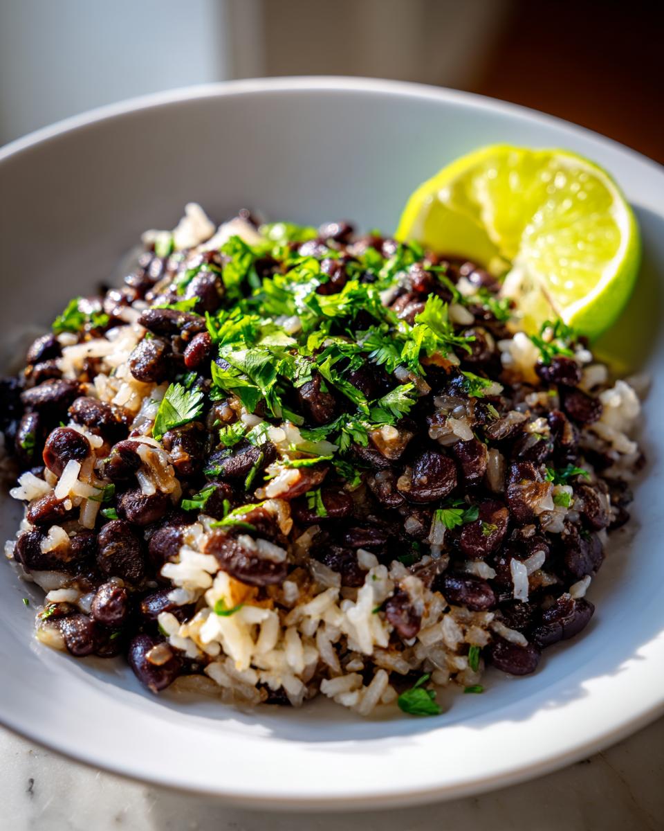 Close-up of a bowl of flavorful black beans and rice topped with fresh cilantro and a lime wedge.