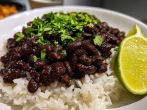 A close-up of a serving of flavorful black beans and rice topped with fresh cilantro and a lime wedge.