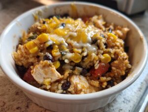 Close-up of a white bowl filled with one pot chicken burrito bowl, featuring rice, chicken, black beans, corn, and melted cheese.