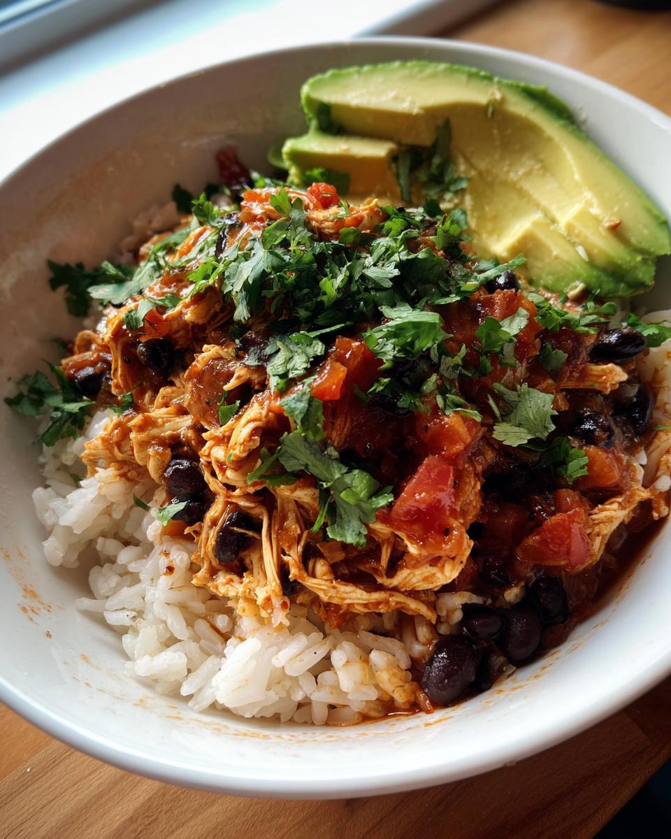 A close-up of a delicious slow cooker chicken burrito bowl featuring shredded chicken, black beans, rice, and topped with fresh cilantro and avocado slices.